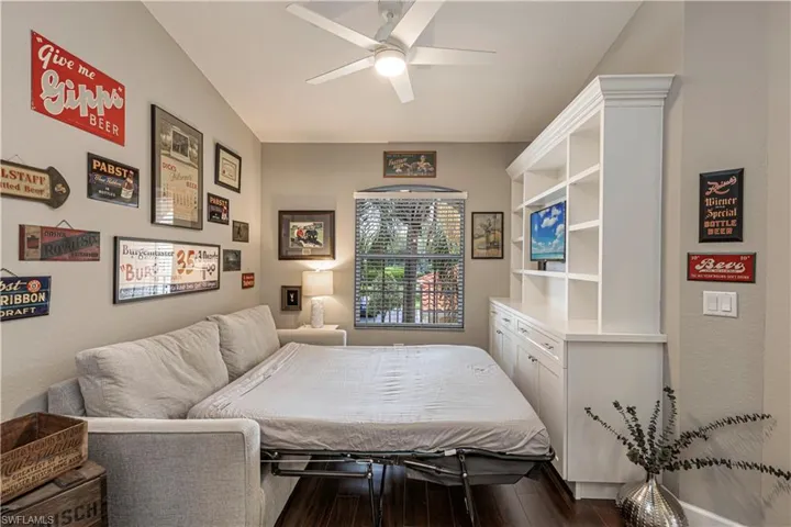 Versatile room featuring a built-in white shelving unit with integrated lower cabinetry, a window with blinds, a ceiling fan, and wood-finish flooring
