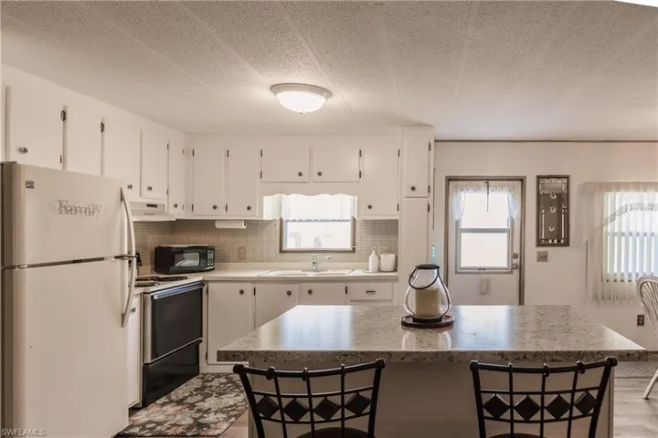 Kitchen featuring a breakfast bar, white appliances, exhaust hood, sink, and white cabinetry