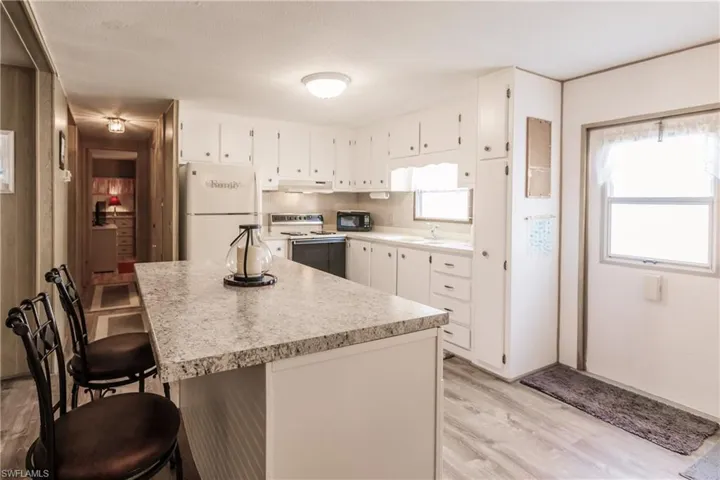 Kitchen featuring a kitchen breakfast bar, a healthy amount of sunlight, white appliances, and and luxury vinyl plank flooring