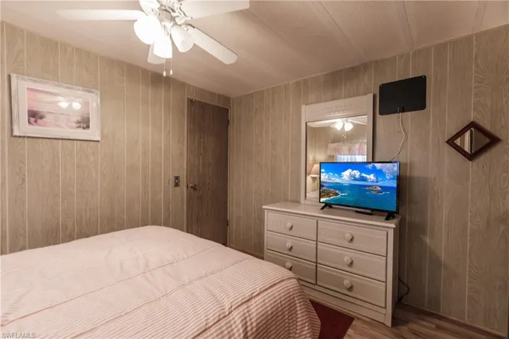 Bedroom with laminate / wood-style floors, ceiling fan, and wood walls