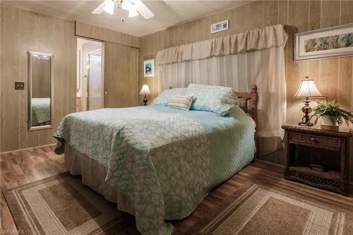 Bedroom featuring laminate / wood-style floors, ceiling fan, and wood walls