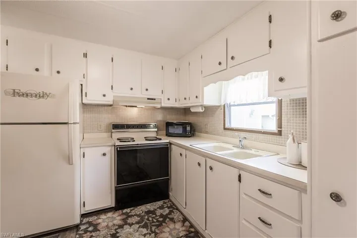 Kitchen featuring tasteful backsplash, white cabinetry, sink, and white appliances