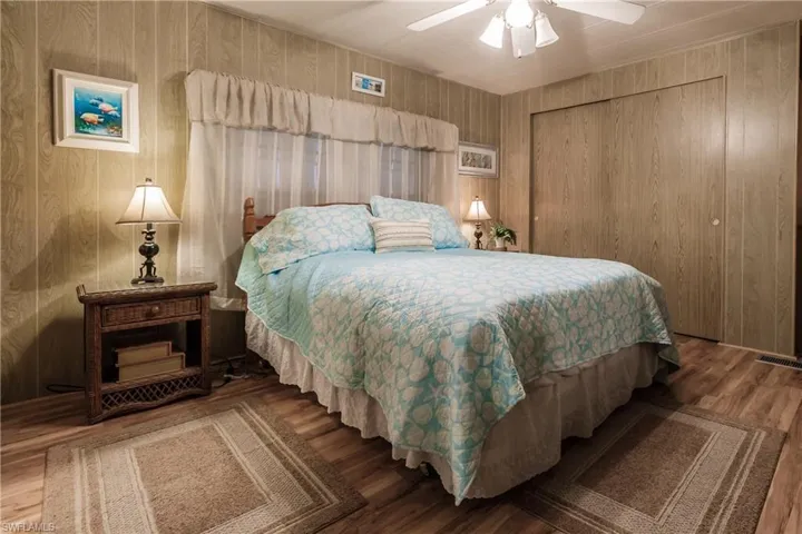 Primary retreat with laminate / wood-style floors, ceiling fan, wood walls, and a closet