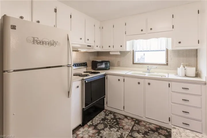 Kitchen featuring white cabinets, white appliances, backsplash, and sink