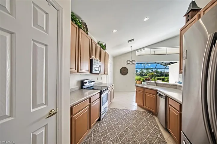 Kitchen featuring vaulted ceiling, light tile patterned floors, stainless steel appliances, decorative light fixtures, and a notable chandelier