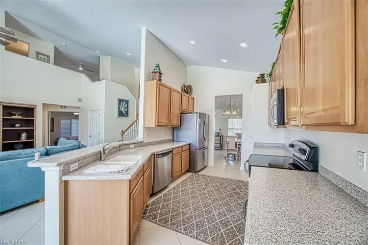 Kitchen featuring appliances with stainless steel finishes, kitchen peninsula, light tile patterned floors, and high vaulted ceiling