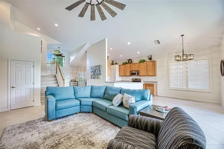 Tiled living room featuring ceiling fan with notable chandelier and lofted ceiling