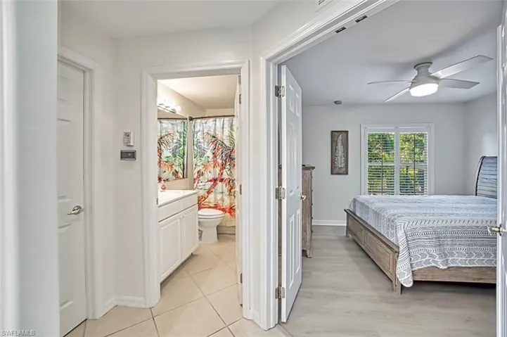 Tiled bedroom featuring ensuite bath and ceiling fan
