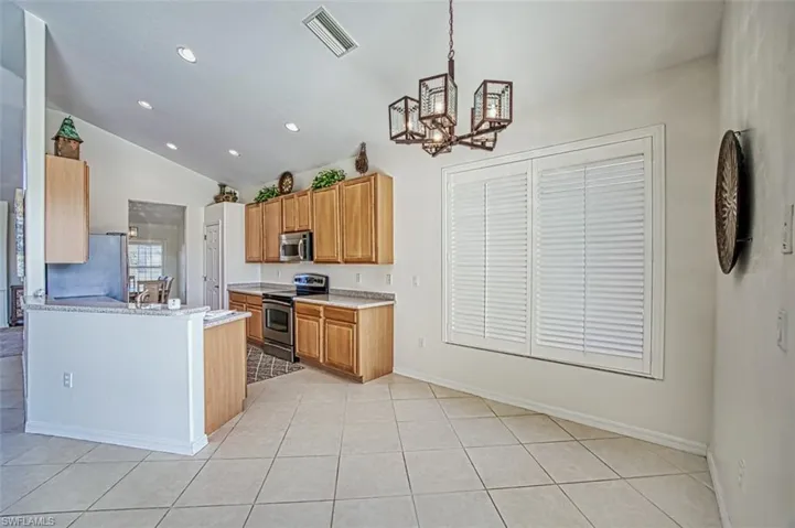 Kitchen featuring appliances with stainless steel finishes, vaulted ceiling, light tile patterned floors, and decorative light fixtures