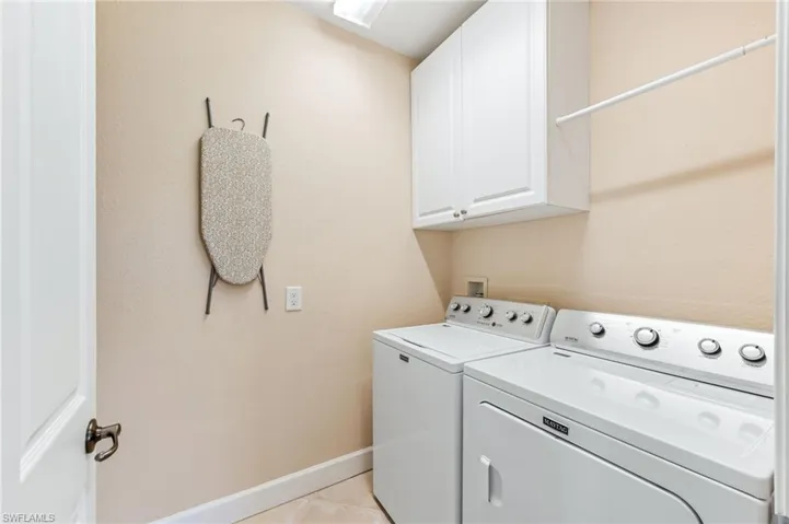Clothes washing area with cabinet space, light tile patterned floors, baseboards, and separate washer and dryer