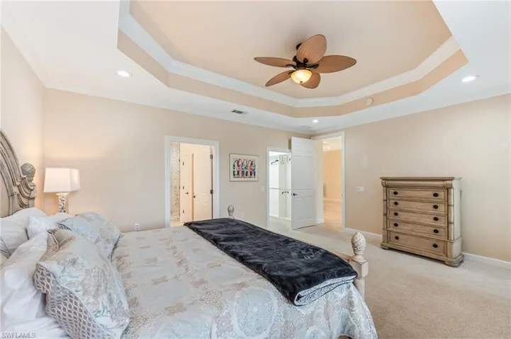 Primary bedroom with ornamental molding, recessed lighting, a tray ceiling, and light colored carpet