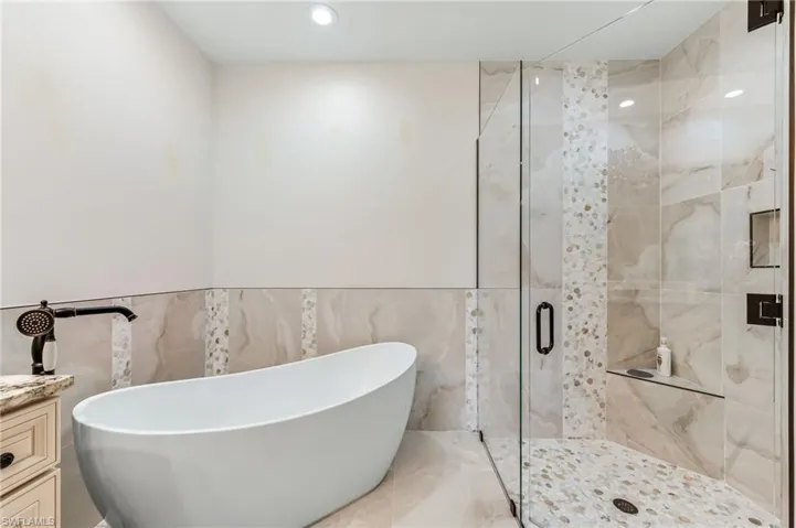 Full bath with a shower stall, a soaking tub, vanity, and tile walls