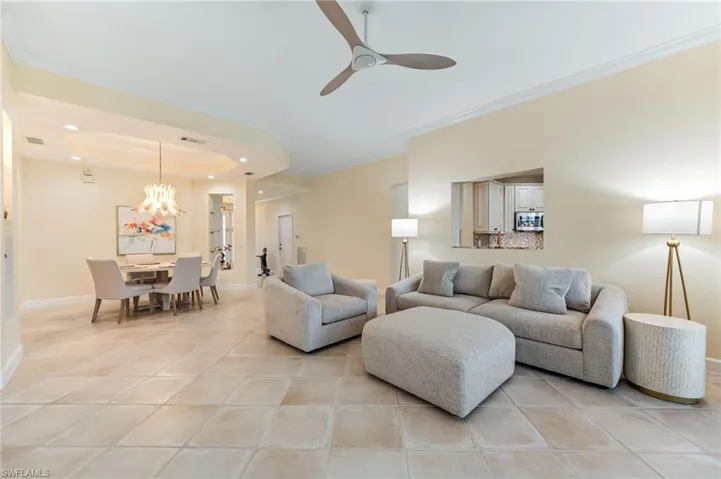 Living room with baseboards, ornamental molding, a tray ceiling, and ceiling fan with notable chandelier