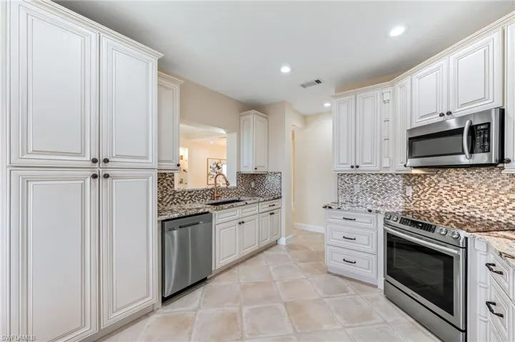 Kitchen with tasteful backsplash, light stone countertops, stainless steel appliances, and a sink