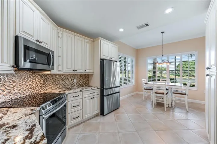 Kitchen featuring a chandelier, backsplash, crown molding, light stone countertops, and appliances with stainless steel finishes