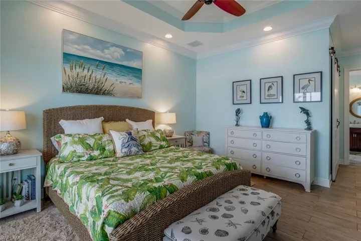 Bedroom featuring porcelain plank tile floors, ceiling fan, a raised ceiling, can lighting and crown molding