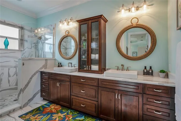 Bathroom with marble tiled shower, ornamental molding, dual vanity, Kraft Maid wood cabinets, and marble flooring