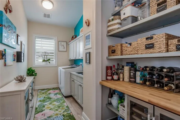 Washroom featuring wine beverage cooler, porcelain plank tile flooring, washing machine and clothes dryer, Kraft Maid cabinets and pantry shelving