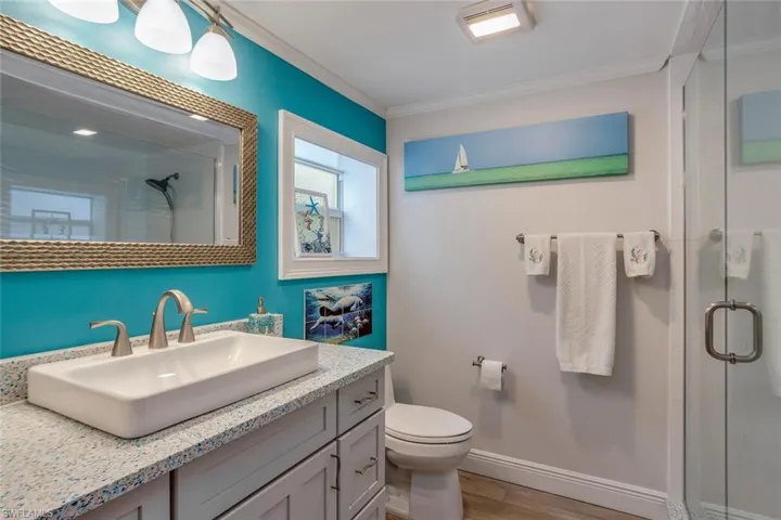 Bathroom featuring a shower with shower door, ornamental molding, porcelain plank tile floor, toilet, and vanity