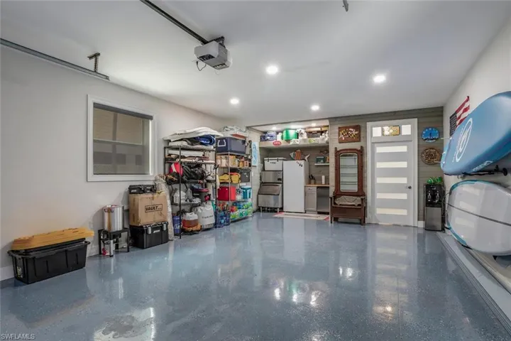 Garage featuring white freezer, ice machine, beverage fridge, cabinet and a garage door opener