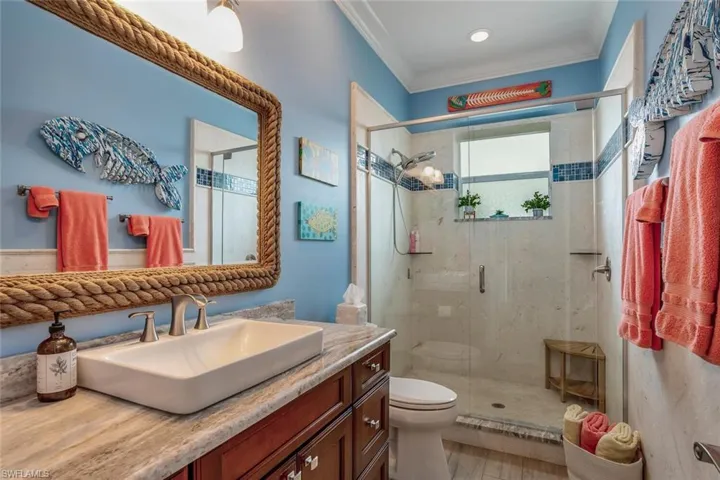 Bathroom with a stone tiled shower with shower door, ornamental molding, Kraft Maid vanity, granite, and toilet