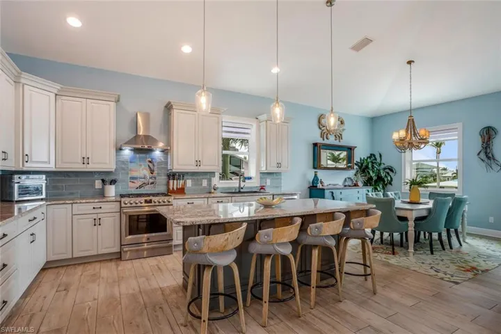 Kitchen featuring decorative light fixtures, high end range, tasteful backsplash with tile mural, and wall chimney exhaust hood