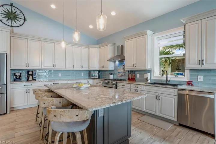 Kitchen with wall chimney exhaust hood, stainless steel appliances, tasteful backsplash with tile mural, and stone sink