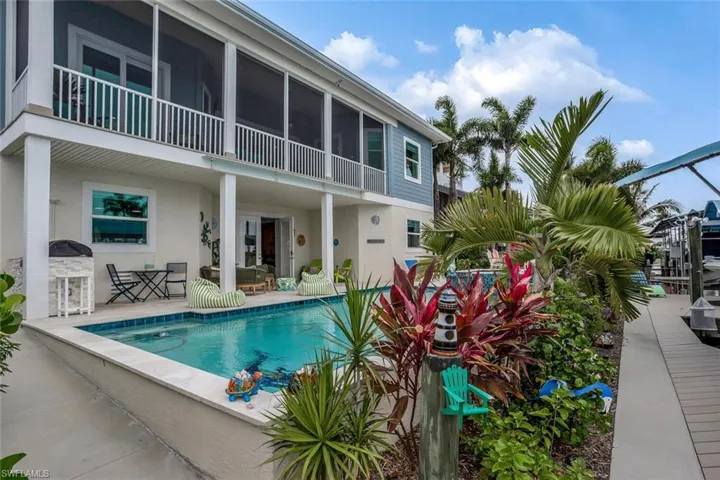 View of saltwater swimming pool featuring a travertine marble patio and built in outdoor kitchen, screened 2nd story balcony