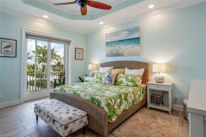 Bedroom featuring ceiling fan, window shades, porcelain plank tile floors, a raised ceiling, access to outside screened balcony, and ornamental molding