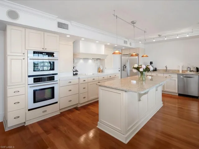 Kitchen with pendant lighting, stainless steel appliances, dark wood-type flooring, light stone counters, and a kitchen bar