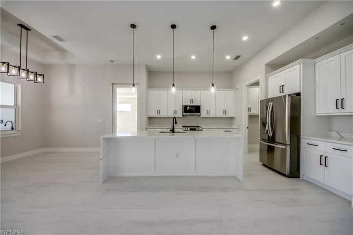 Kitchen featuring stainless steel appliances, an island with sink, white cabinetry, light stone counters, and recessed lighting