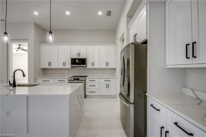 Kitchen featuring light stone countertops, appliances with stainless steel finishes, white cabinetry, hanging light fixtures, and recessed lighting