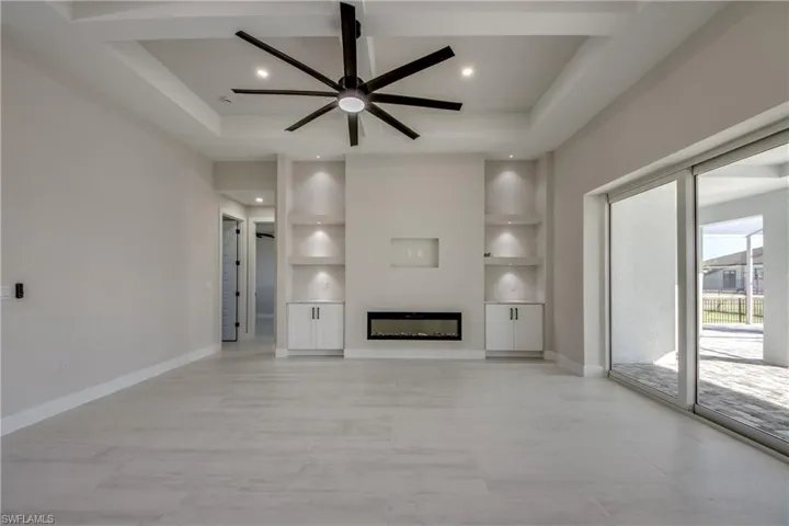 Unfurnished living room with built in shelves, a glass covered fireplace, a ceiling fan, a raised ceiling, and recessed lighting