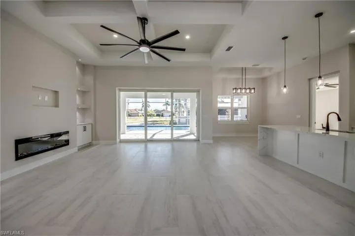 Unfurnished living room with a ceiling fan, built in shelves, plenty of natural light, coffered ceiling, and light wood-style floors