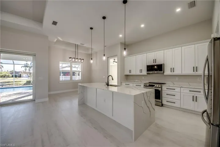 Kitchen with stainless steel appliances, light stone countertops, white cabinetry, a kitchen island with sink, and recessed lighting