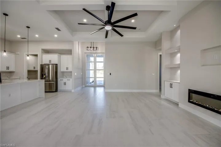 Unfurnished living room with ceiling fan, a glass covered fireplace, built in features, a tray ceiling, and recessed lighting