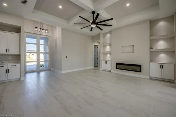 Unfurnished living room with coffered ceiling, a glass covered fireplace, built in shelves, french doors, and ceiling fan