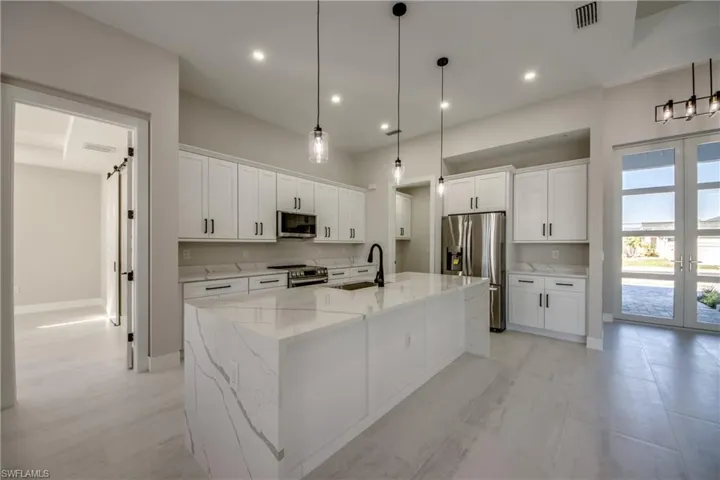 Kitchen featuring light stone countertops, appliances with stainless steel finishes, white cabinetry, a center island with sink, and hanging light fixtures