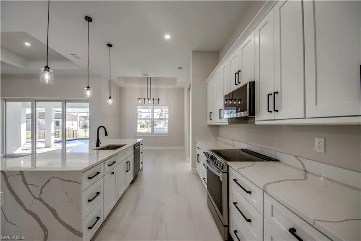 Kitchen with light stone counters, stainless steel appliances, hanging light fixtures, white cabinets, and recessed lighting