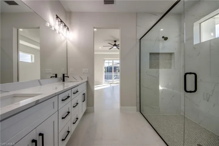 Full bath featuring double vanity, a marble finish shower, and a ceiling fan