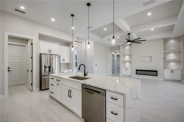 Kitchen with white cabinetry, coffered ceiling, open floor plan, decorative light fixtures, and light stone counters