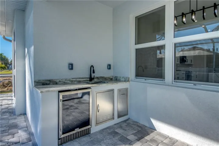 Bar area with beverage cooler, light stone counters, a textured wall, white cabinetry, and stone finish flooring