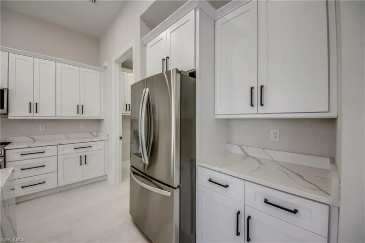 Kitchen with stainless steel appliances, light stone counters, and white cabinetry
