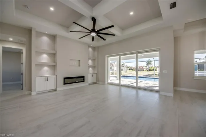 Unfurnished living room with built in shelves, coffered ceiling, a glass covered fireplace, beam ceiling, and a ceiling fan