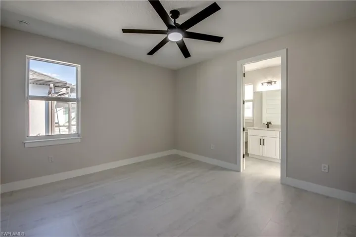 Unfurnished bedroom with ceiling fan, multiple windows, and ensuite bath