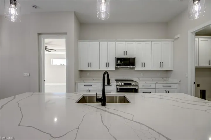Kitchen with light stone counters, white cabinetry, decorative light fixtures, and appliances with stainless steel finishes