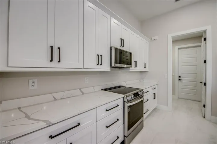 Kitchen featuring stainless steel appliances, light stone countertops, and white cabinets