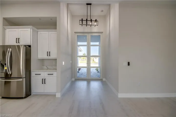 Kitchen featuring stainless steel fridge, white cabinets, french doors, and pendant lighting