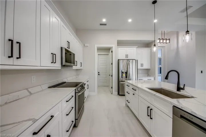 Kitchen featuring light stone counters, appliances with stainless steel finishes, white cabinetry, pendant lighting, and recessed lighting