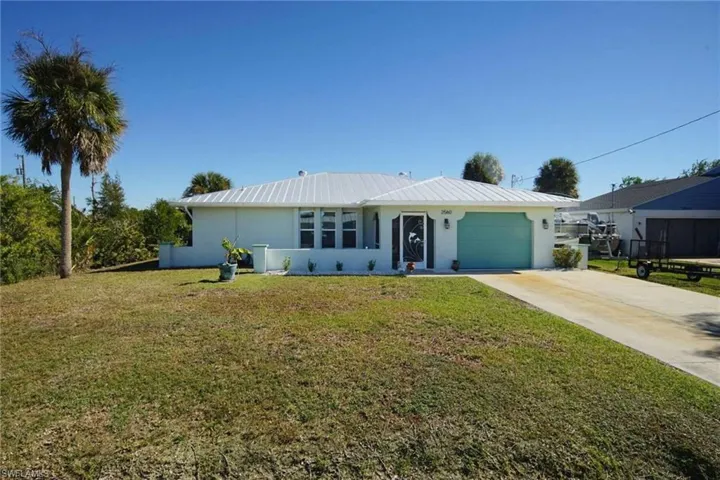 Single story home featuring a garage, stucco siding, a front yard, driveway, and a metal roof
